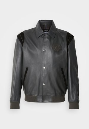 Black leather jacket with a smooth texture, snap button closure, side pockets, ribbed cuffs and hem, and a patch detail on the chest.