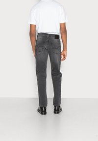 Jeans de mezclilla gris con ajuste slim, diseño de cinco bolsillos y pierna recta. Parche de cuero negro en la cintura, combinados con una camiseta blanca.