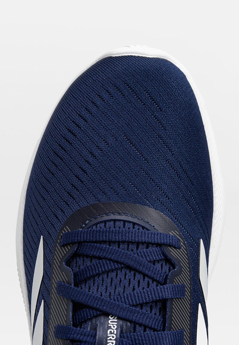 Zapatilla deportiva de punto en azul con suela blanca. Las características incluyen cordones planos, una parte superior texturizada y un contrafuerte en el talón que proporciona soporte.