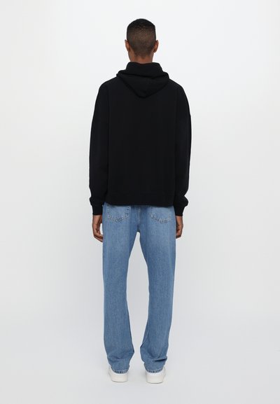 Sweatshirt à capuche noir avec une coupe décontractée, associé à un jean large bleu clair et des baskets blanches. Texture lisse, design minimaliste.