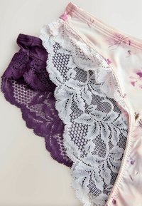 Divas sieviešu biksītes ar mežģīnēm, vienas gaiši rozā ar ziedu rakstu un baltām mežģīnēm, otras violetas ar atbilstošām violeta mežģīnēm, izklātas plakani.