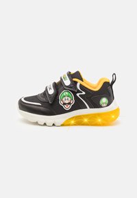 Zwarte sportieve schoen met gele zool, klittenbandsluitingen en cartoonfiguuraccenten. Heeft een gestreepte bovenkant en kleurrijke details.