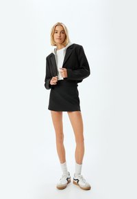 Zwarte cropped jas over een witte top, gecombineerd met een zwarte mini rok. Witte sneakers met grijze accenten en gestructureerde kniehoogsokken.