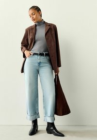 Brauner Wildlederblazer, grauer Rollkragenpullover, hellblaue weite Jeans mit umgeschlagenen Säumen, schwarze strukturierte Stiefeletten, in der Hand eine braune Tote-Tasche.