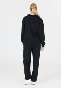 Zwarte hoodie en bijpassende joggingsbroek van zacht materiaal. Voorzien van een capuchon en een relaxte pasvorm; eenvoudige stijl zonder zichtbare patronen.