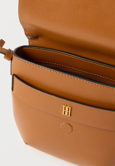 Ταμπά δερμάτινη τσάντα χιαστί με ανοιχτό καπάκι, που δείχνει το ραμμένο εσωτερικό και το χρυσό λογότυπο μπροστά.