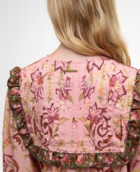 Rochie cu model floral pe un fundal roz, cu margini ondulate verzi și un spate texturat care prezintă cusături verticale și un mic eticheta metalică.