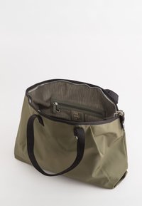 Oliwkowa torba tote z czarnymi uchwytami, otwarta u góry, z widoczną wewnętrzną kieszenią na zamek i etykietą "FRIENDLY" w środku.