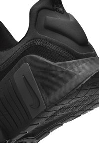 Černá sportovní obuv s texturovanou tkaninou a gumovou podrážkou. Vyznačuje se výrazným logem Nike a polstrovanou zadní částí pro podporu.