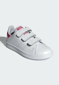 Baskets en cuir blanc avec trois bandes Velcro, accents roses sur le talon et la languette, détails perforés sur les côtés et semelle en caoutchouc.