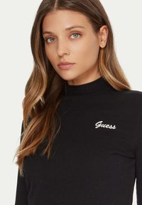 Top nero a maniche lunghe con collo alto, con logo "Guess" ricamato in bianco sul petto. Realizzato in materiale liscio ed elastico.