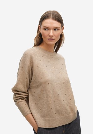 Suéter de punto beige con cuello redondo, corte relajado y decorado con pequeños remaches dorados en la parte frontal y las mangas.