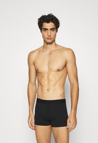 Zwarte boxershorts met een effen kleur ontwerp, elastische tailleband en een aangesloten pasvorm, gedragen door een model met een blote torso.
