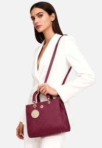 Borsa color bordeaux con texture trapuntata diagonale, doppie maniglie superiori e tracolla rimovibile. Caratterizzata da dettagli in oro e logo.