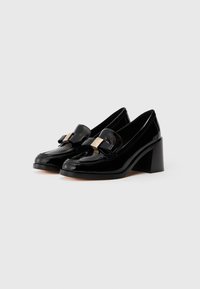 Crne lakirane kožne cipele na petu u obliku loafersa sa četvrtastim vrhom, s ukrasnom mašnom i metalnim detaljem na gornjem delu. Dizajn s masivnom petom.