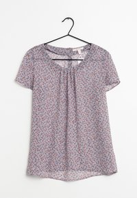 Blusa leggera azzurro chiaro a maniche corte con piccolo motivo floreale rosso e bianco, scollatura tonda con parte anteriore plissettata, appesa a un appendiabiti nero.
