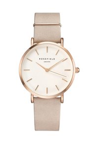Montre ronde avec un bracelet en cuir suédé beige, un boîtier en or rose, un cadran blanc, des index horaires simples et deux aiguilles fines. Logo de la marque visible.