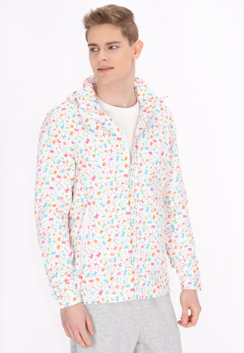 Giacca leggera con zip su sfondo bianco e motivo a foglie colorate in rosa, blu e verde. Presenta un colletto alto e tasche laterali.