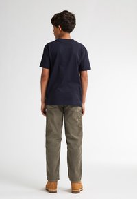 Marineblauw katoenen t-shirt gecombineerd met olijfgroene cargobroek. De outfit heeft een losse pasvorm en praktische zakken. Bruine schoenen maken de look compleet.