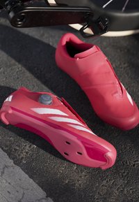 Czerwone buty rowerowe wykonane z materiałów syntetycznych o smukłym designie. Funkcje obejmują zapięcie na pokrętło i białe paski, z gładką podeszwą.
