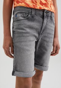 Šedé džíny kraťasy s ohrnutým lemem, s pěti kapsami a mírným vyblednutím. Modrý akcent na přední kapse.