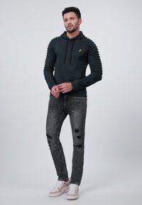 Hanorac negru texturat cu mâneci ribbed, asociat cu blugi gri distresați și adidași albi cu accente roz. Logo auriu pe hanorac.
