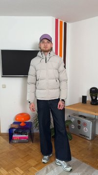 Ανοιχτό γκρίζο μπουφάν με φερμουάρ, μαύρες λεπτομέρειες και κουκούλα, σε συνδυασμό με φαρδιές σκούρες τζιν παντελόνες και γκρι αθλητικά παπούτσια.