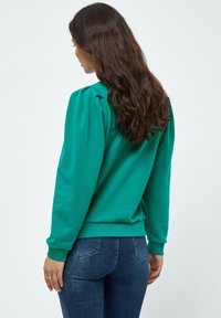 Felpa color teal con maniche a sbuffo e polsini a costine. Realizzata in materiale morbido, presenta un orlo aderente e un design semplice, privo di decorazioni.
