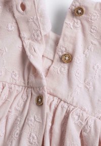 Pink fabric dress featuring floral embroidery, two wooden buttons, and gathered detail at the waist. Soft texture with a subtle sheen.