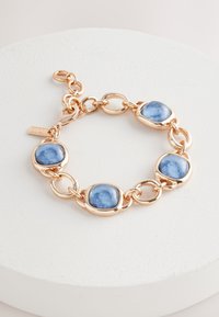 Brass bracelet with gold-tone finish featuring four round blue resin stones, each encased in a smooth, bezel-like setting.