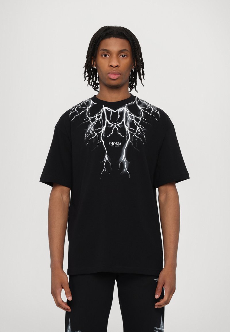 T-shirt in cotone nero con una grafica di un fulmine bianco sulla parte anteriore e il testo "PHOBIA" centrato sotto il design. Maniche corte.