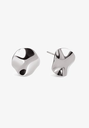 Paire de boucles d’oreilles clous en métal argenté brillant, de forme irrégulière, avec des surfaces lisses et réfléchissantes et une tige courte pour fixation.