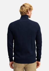 Granatowy sweter z prążkowanej dzianiny, z wysokim kołnierzem i dopasowanymi mankietami. Projekt ma fakturowany wzór i luźny krój.