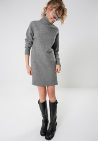 Gray knitted sweater dress with a high collar and ribbed cuffs, paired with knee-high black leather boots featuring buckles.