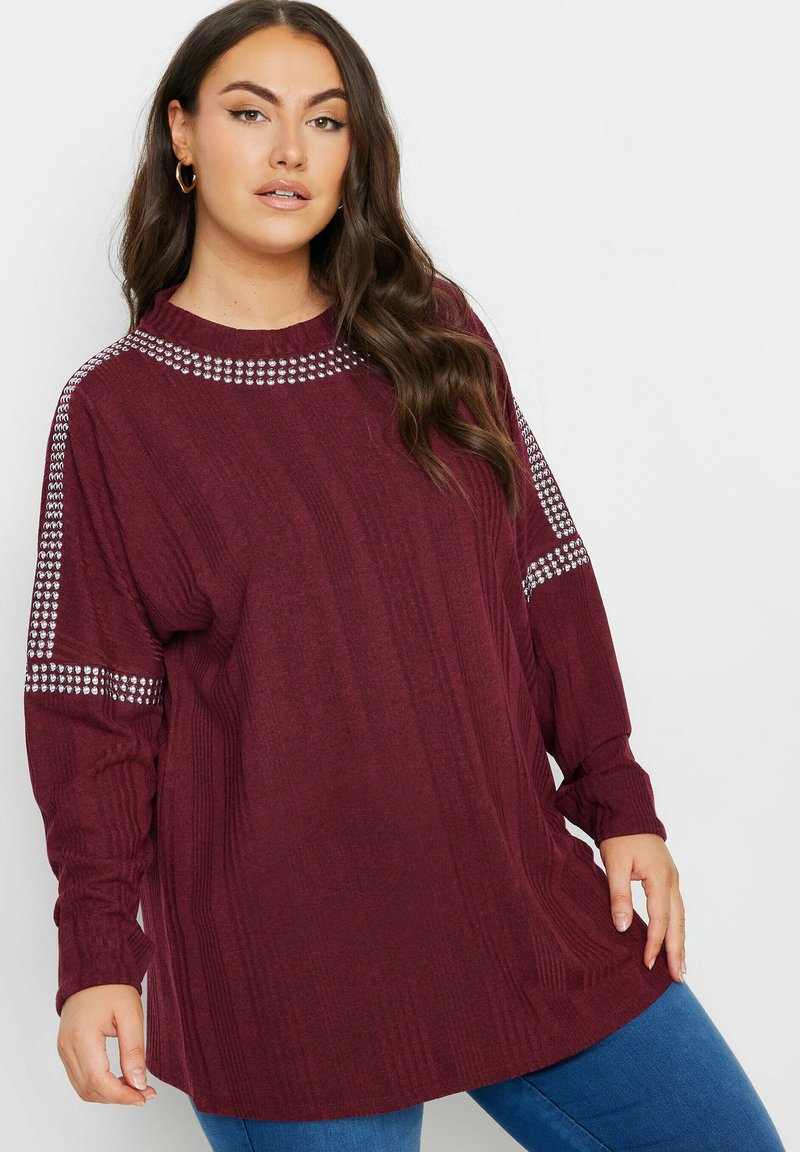 Burgundy stickad långärmad tröja med ribbad textur och utsmyckad axeldesign. Löst sittande, rund halsringning och höftlång längd.