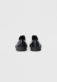 Zapatos de cuero negro con un acabado suave, de perfil bajo y puntera redonda. Presentan una suela acolchada y un diseño minimalista sin hardware visible.