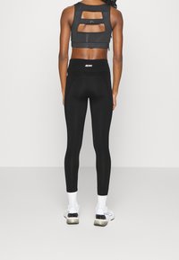 Černé sportovní legíny s vysokým pasem, spárované s černým crop topem s texturou a výřezem na zádech. Bílé ponožky a sportovní boty.