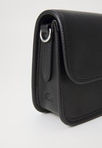 Black leather shoulder bag with a textured surface, rounded edges, a flap closure, and a silver hardware accent. Features embossed logo.