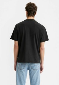 Juodas medvilninis t-shirt su trumpomis rankovėmis, apvalia iškirpte, lygia tekstūra ir laisvu siluetu, derinamas su šviesiai mėlynos denimo kelnėmis.