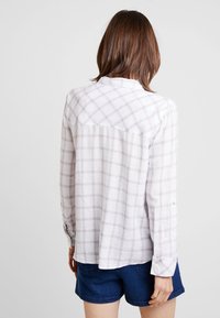 Chemise à carreaux blancs avec des lignes violettes claires, manches longues et poignet boutonné ; tissu léger avec une surface légèrement texturée.