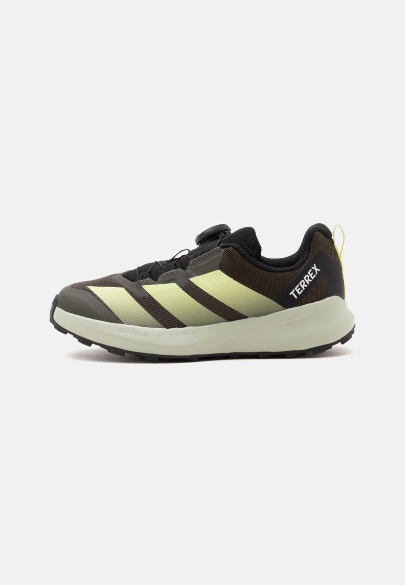 Μαύρο και ελιά πράσινο παπούτσι τρεξίματος Adidas Terrex με ανοιχτόχρωμη σόλα και κουμπί ρύθμισης κορδονιών σε λευκό φόντο.