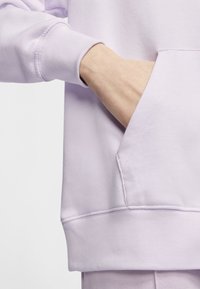 Lavendelfärgad sweatshirt med ficka, med ribbad mudd och nederkant. Materialet verkar mjukt med en slät textur och minimal sömnadsdetalj.