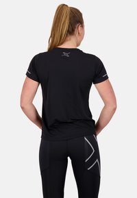Maglietta sportiva nera a maniche corte con scollo rotondo, caratterizzata da un logo riflettente sul retro e dettagli sottili sulle maniche.