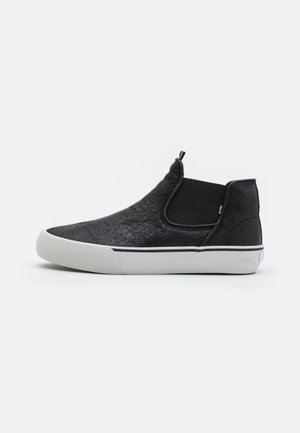 Black slip-on shoes featuring a textured upper material, elastic side panels, and a white rubber sole with a subtle black stripe accent.