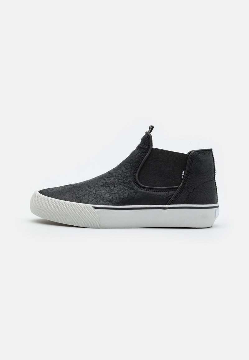 Zapatos negros tipo slip-on con material superior texturizado, paneles laterales elásticos y una suela de goma blanca con un sutil acento de franja negra.