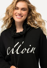 Felpa nera con collo a cowl e coulisse, caratterizzata da testo in bianco scritto a mano. Tessuto morbido, vestibilità comoda e design minimalista.