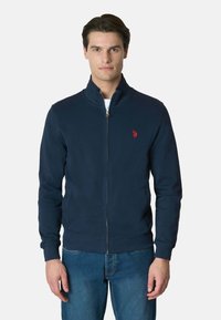 Felpa navy con zip in tessuto morbido, dotata di colletto alto, polsini a coste e un piccolo logo rosso sul petto.