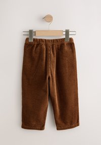 Hnedé kordurové nohavice s vertikálnou rebrovanou textúrou, vybavené elastickým pásom a dizajnom s priamymi nohavicami, zavesené na drevenom klipovom vešiaku.