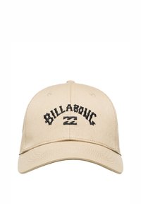 Beige bomulds cap med en buet skygge, der har sort broderet tekst "BILLABONG" og et centreret logodesign. Justerbar strop på bagsiden.