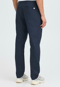 Pantalons en coton bleu marine avec une coupe droite, poches arrière et une petite étiquette de marque sur la taille. Tissu texturé.